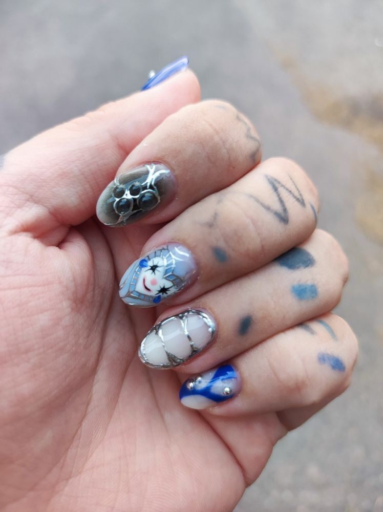 Picture of Aleka's hand, showing his nails. The nails are futuristic, blue, black and chrome. Middle finger has a heart shaped clown look.