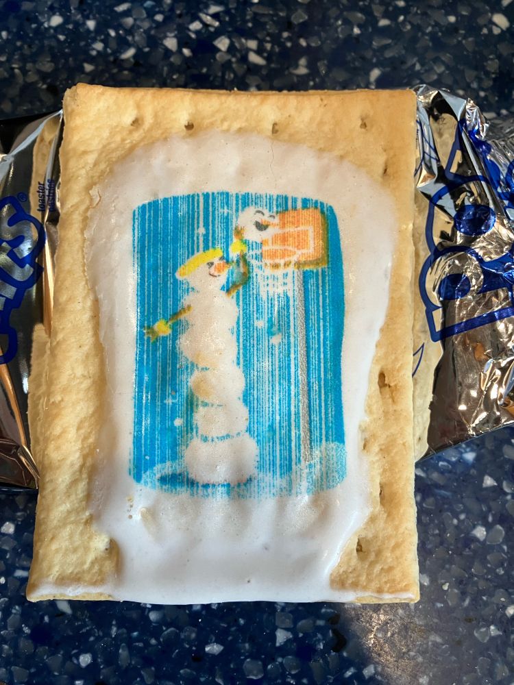 Sugar Cookie poptart with image of one snowman dunking the head of the other through a basketball hoop, which it reaches, presumably, by standing on the body of the one it is dunking. Both heads are smiling, the dunked head more broadly.
