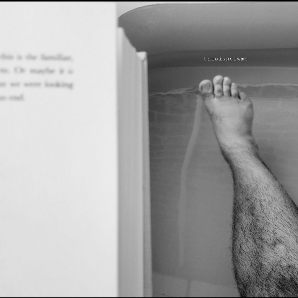 Black and white photo of my size 13 Puerto Rican male foot on one half of the picture and a book wth blurry text on the left. Watermarked with thisisnsfwme.