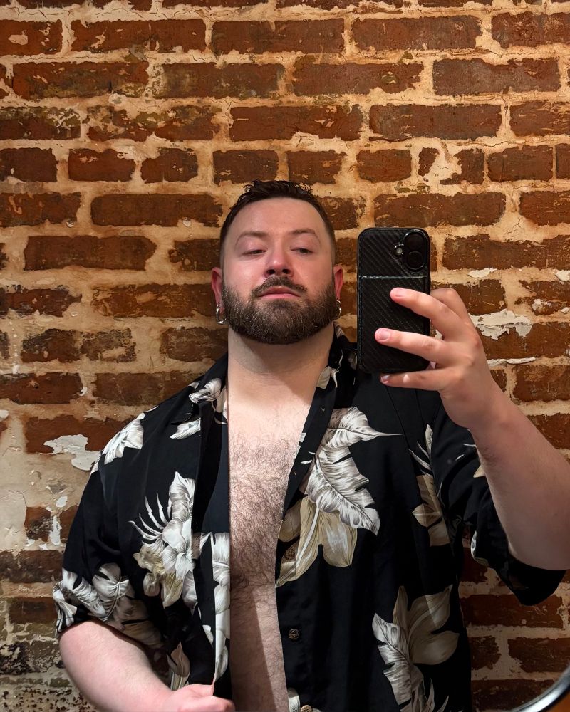 Drunk scruffy bear in a pseudo Hawaiian shirt taking a mirror selfie 