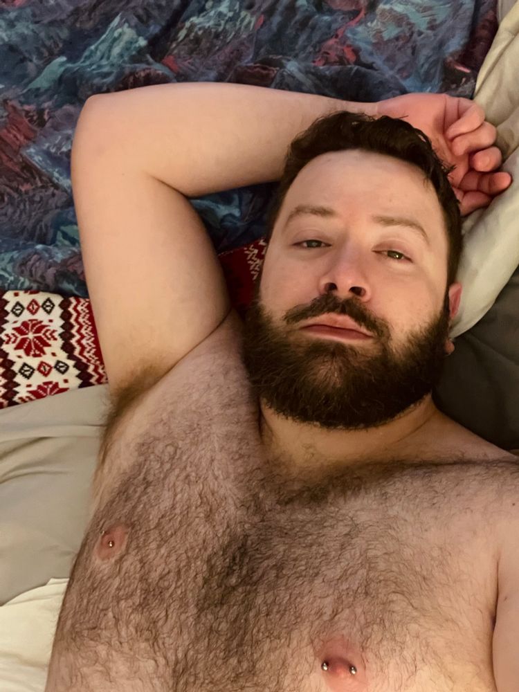 A tired medium closeup selfie featuring my sleepy face and hairy chest (pierced nipples and all). 