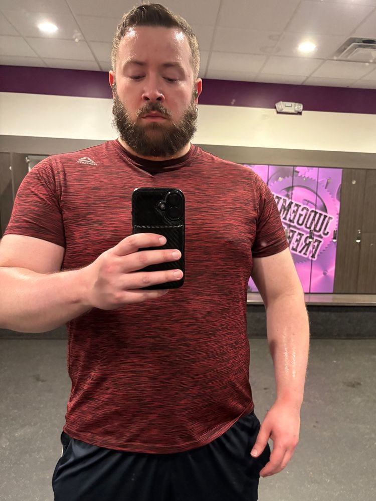 Mirror gym selfie of me (an exhausted sweaty hairy gay) wearing a dark red/maroon heathered shirt and navy gym shorts) in an empty locker room. 