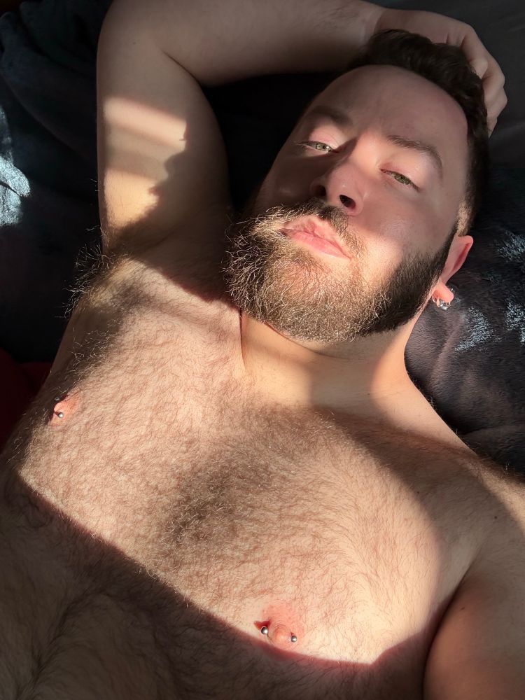 Lazy selfie of me in bed with the sun casting dramatic light across my face and hairy bare chest