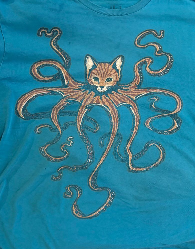 A blue t-shirt bearing the faded graphic of an octopus with the head of a cat and tabby patterning.
