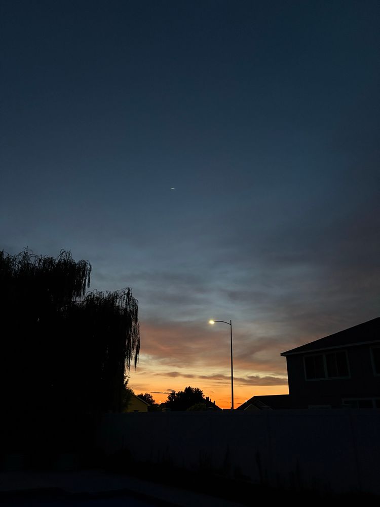 Phot of a sunset. There is a streetlight in the center of the frame with a silhouette of a tree on the left and the silhouette of a house on the right.