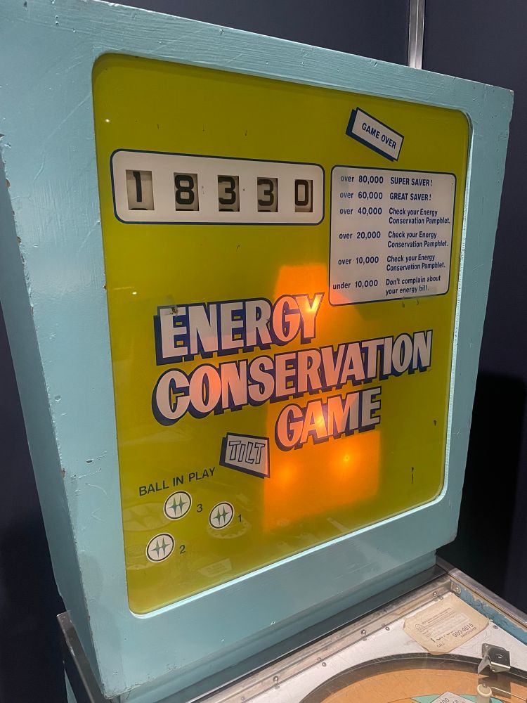 The top marquee of the pinball game. “Energy Conservation Game” in white lettering on a yellow background with a baby blue border.