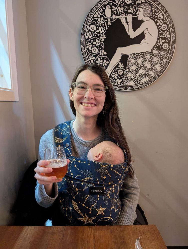 Davis raises a glass of beer with a sleeping baby in a carrier. 