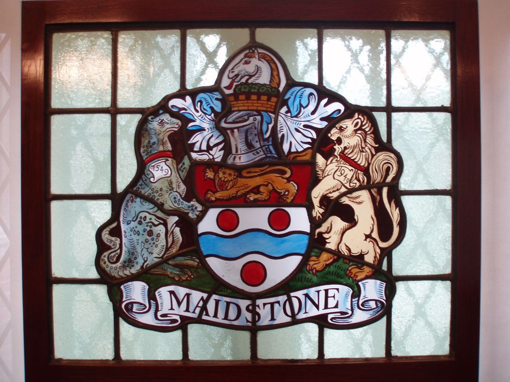 Arms: Or a Fesse wavy Azure between three Torteaux on a Chief Gules a Lion passant guardant Or.
Crest: Issuant from a Mural Crown Or a Horse's Head Argent gorged with a Chaplet of Hops fructed proper, Mantled Azure doubled Or.
Supporters: On the dexter side an Iguanodon proper collared Gules and on the sinister side a Lion Or collared Gules.