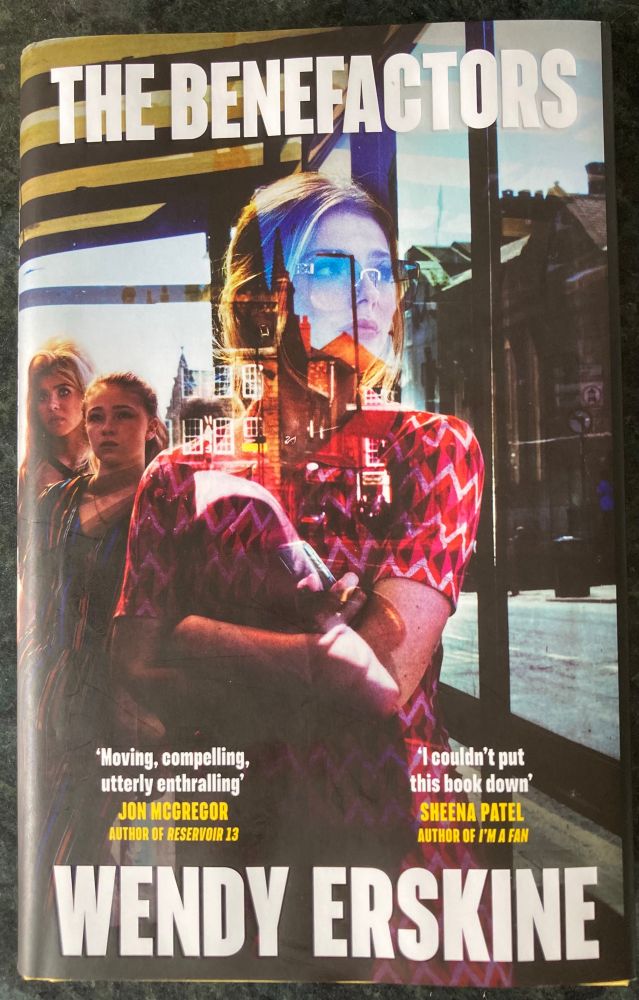 Book cover - The Benefactors by Wendy Erskine - feat photo of woman in pink/red dress in what looks to be a bus stop, with people in background 
