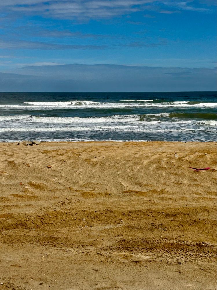 Sandy beach with gentle waves and a blue sky with wispy clouds