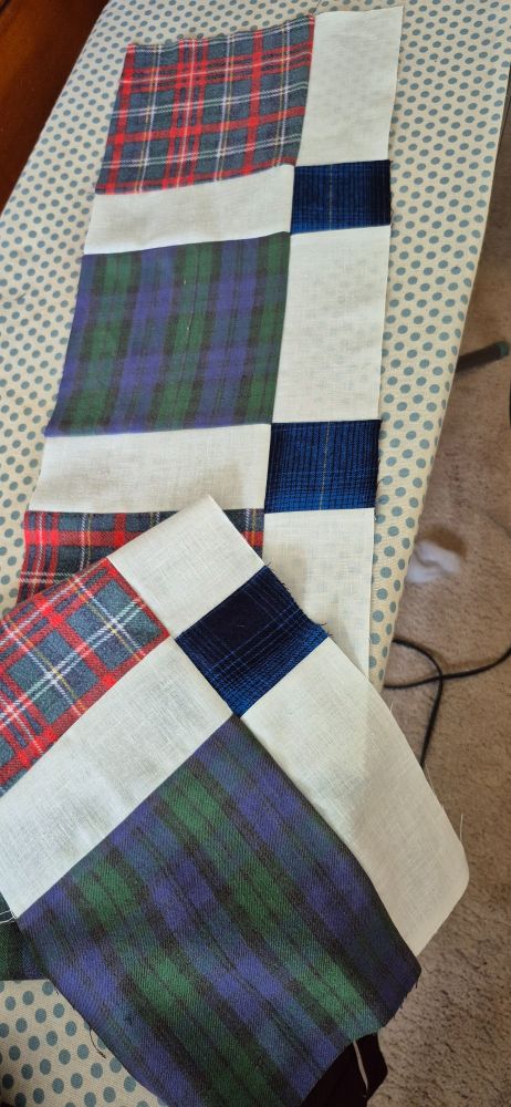 2 rows of flannel quilts squares sewn together with white muslin. The flannel is a red, white, and blue plaid; a green and blue plaid; and a dark blue and black plaid.