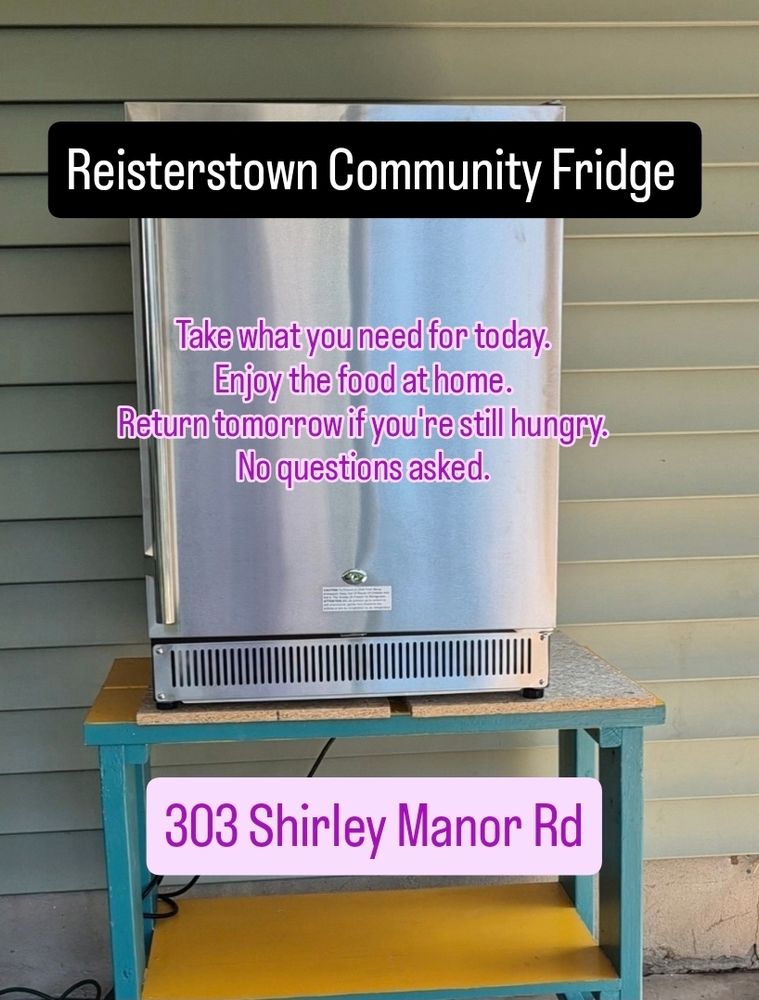 An large outdoor mini fridge sitting on top of a wooden table. Text: Reisterstown Community Fridge.  Take what you need for today. Enjoy the food at home return tomorrow if you're still hungry. No questions asked. 303 Shirley Manor Rd.