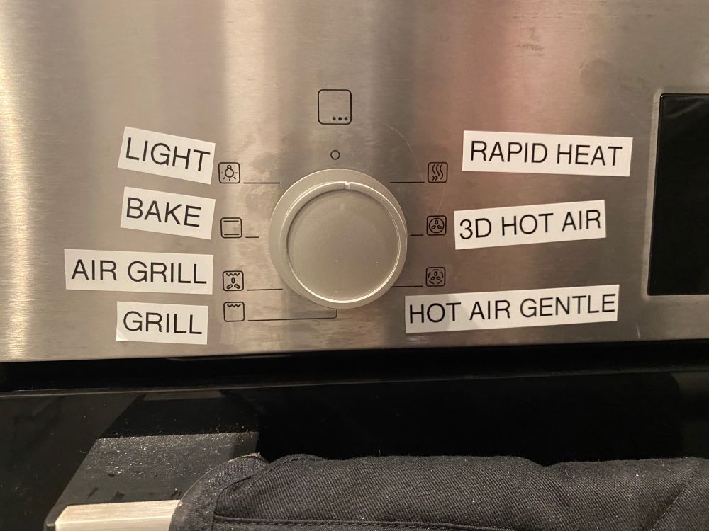 A picture of an oven mode selector where large ugly white labels have been stuck on it so you easily know if you are baking or grilling. 