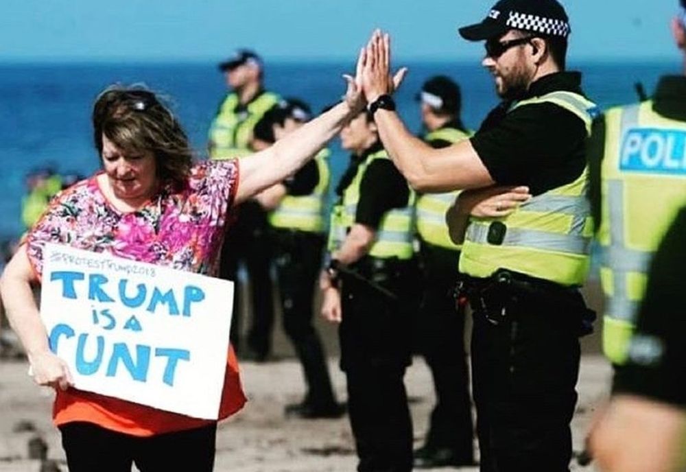 photo of Janey Godley with her "Trump is a Cunt" sign, being high-fived by a policeman in the security detail