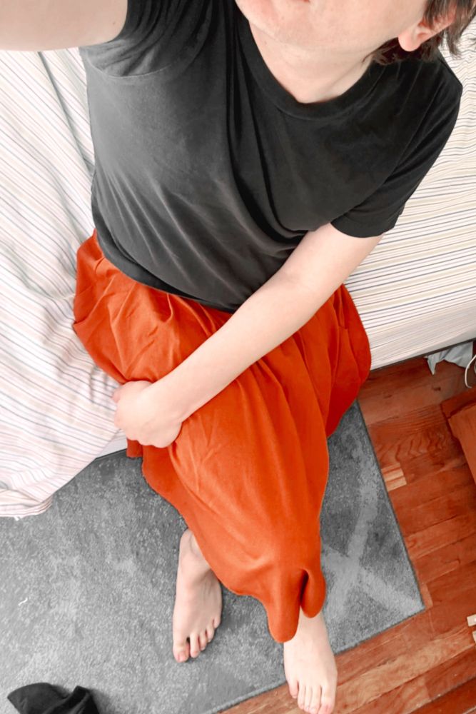 Me sitting on a bed wearing a simple black t-shirt top and a red/orange wool skirt, photo taken from a high angle looking down 