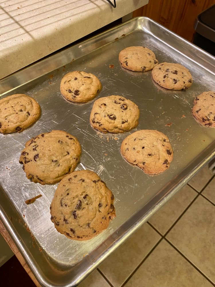 a silver cookie sheet with nine chocolate chip cookies on it.