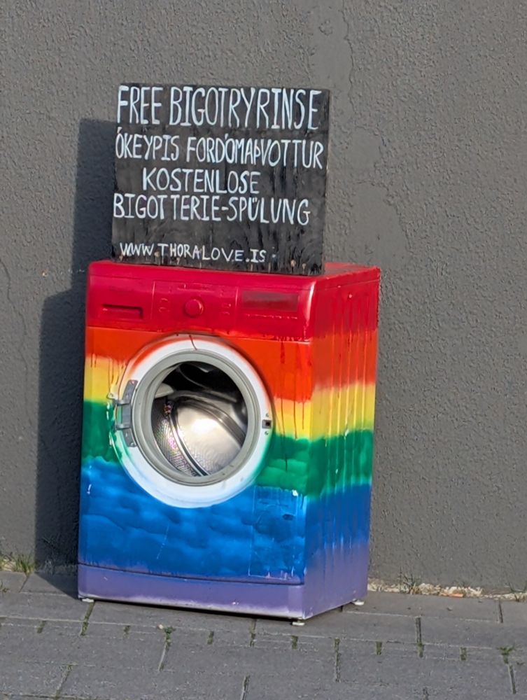 A washing machine in the streets of Akureyri, Iceland. It's painted in rainbow colors and has a sign saying "Free bigotry rinse"