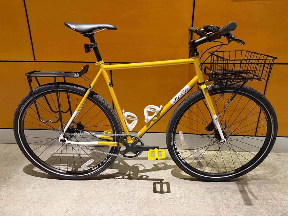 Side profile of the yellow All-City Super Professional with yellow petals, a black rear rack, and black front rack and basket.