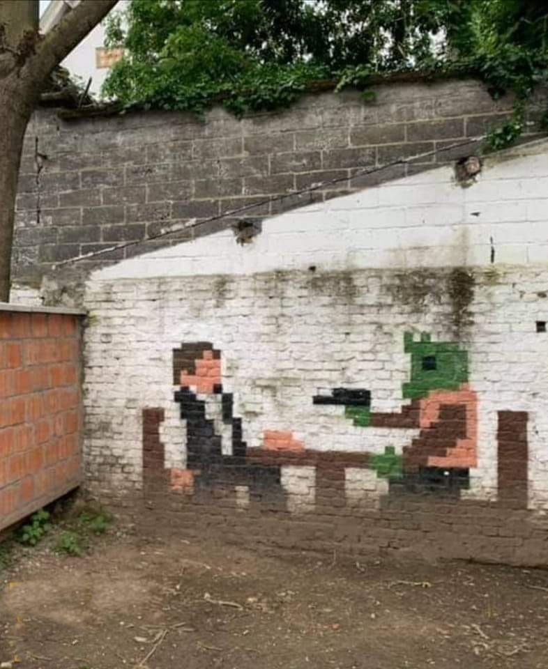 A brick wall, and the bricks have been painted to represent a less than 8 bit rendering of Greedo pulling his gun on Han Solo in the Mos Eisley Cantina from the original Star Wars motion picture 