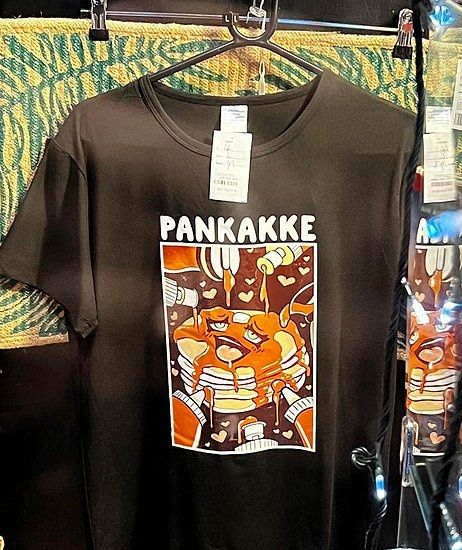 A t-shirt depicting pancakes doing an aheago face while being slathered on by lots of syrup from all angles, pankakke