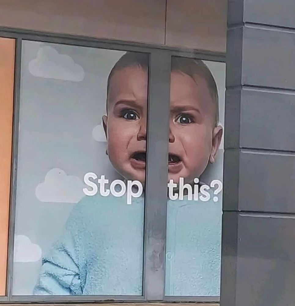 A poster of a crying baby that says "stop this?" and there's more context over to the left but isolated and with a structural beam splitting the image in two making the baby look demented and crazed and immediately funny and off putting