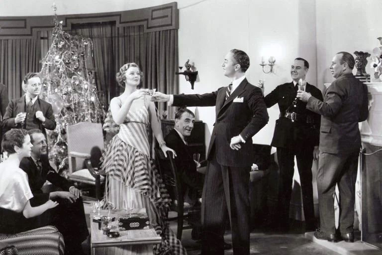 Myrna Loy and William Powell in The Thin Man (1934). As Nick and Nora Charles, they are hosting a Christmas Eve party at their Manhattan apartment. Their Christmas tree is in the background, they are offering a toast surrounded by several of their friends. 