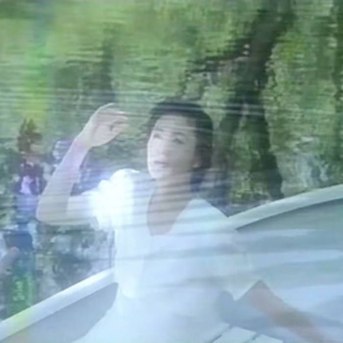 Cover art to part 3 of ‘Spiritual Ascension’ by m e m o r y メモリー. A fuzzy shot of a Japanese woman dressed all in white, possibly sitting in a white rowboat. In the background we see trees and plants reflected in open water.