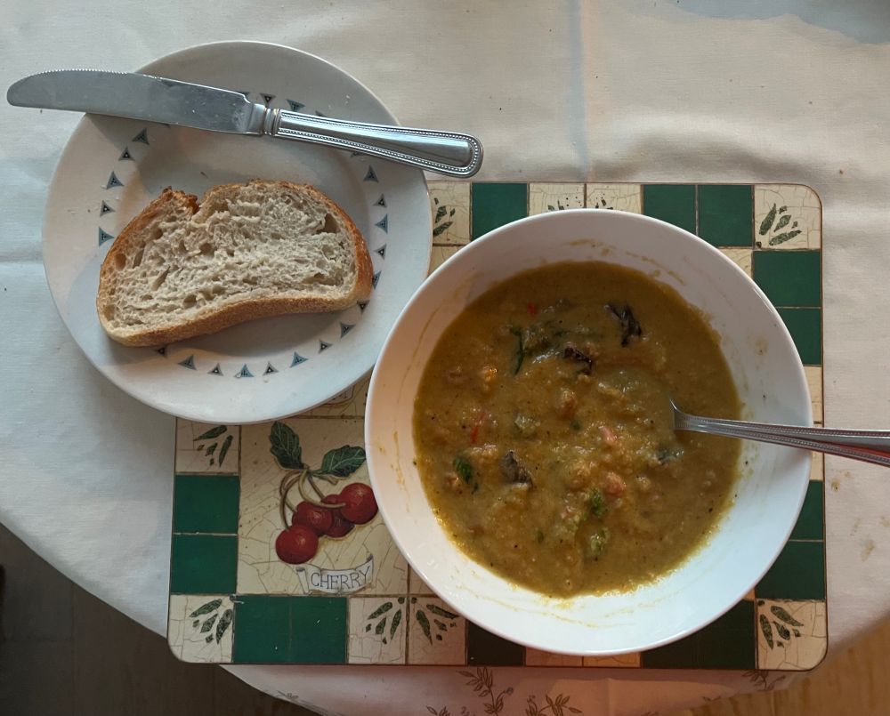 A half-eaten bowl of chickpea and chard soup, with a slice of bread on the side.