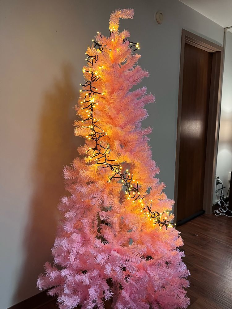 A light pink Christmas tree with tree lights going around the tree. 
