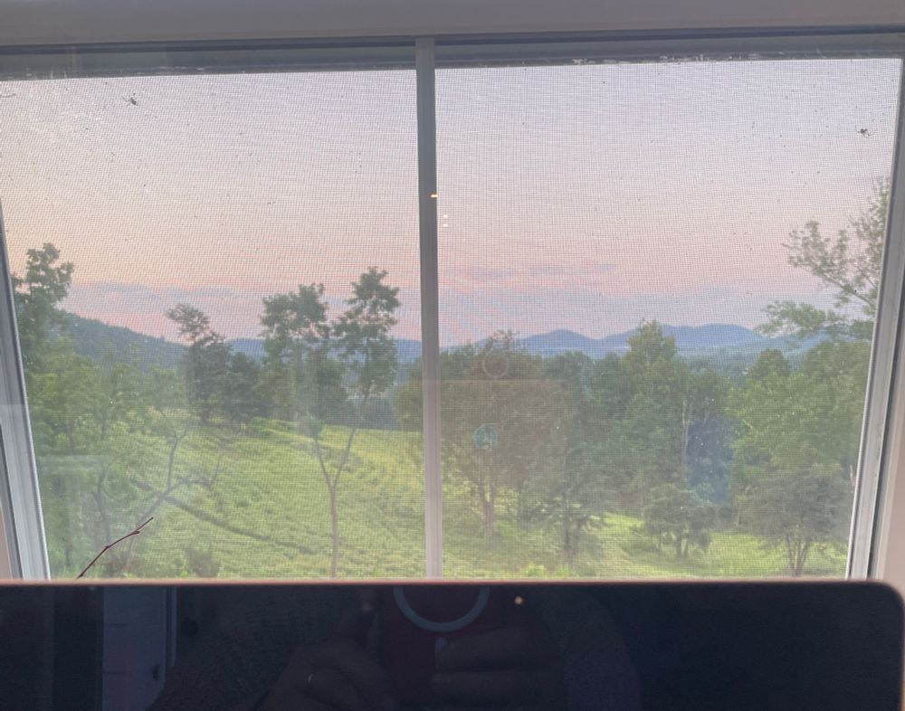 A view out a window showing misty mountains. Top of a laptop can be seen in picture.