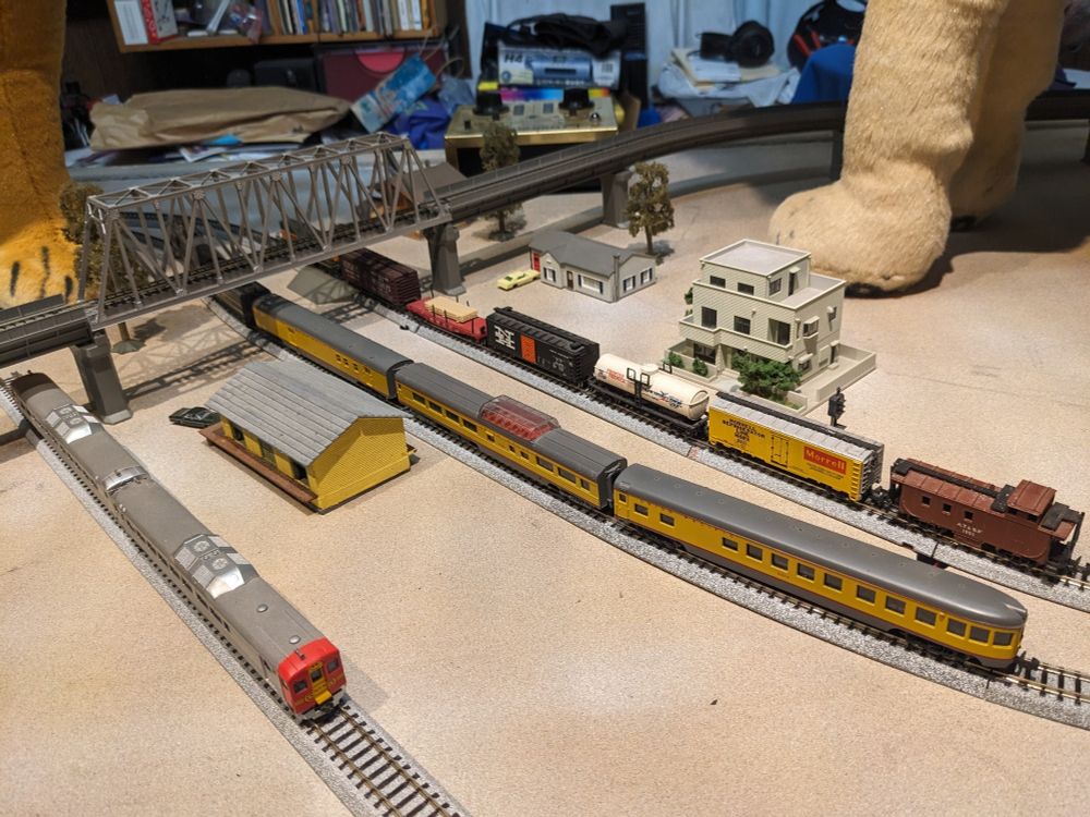 Photo of model trains. A freight train with various cars, a passenger train with steam locomotive and observation cars and a pair of rail diesel cars.