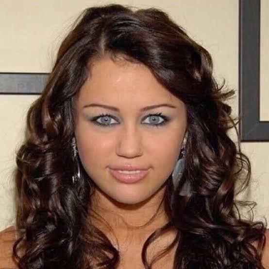 famous meme picture of miley cyrus with her striking blue eyes staring directly into the camera with an emotionless half smile and she kinda looks a bit unhinged