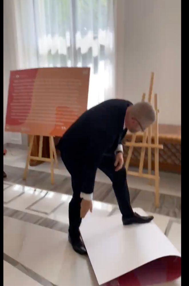 Mann im Anzug (Grezgorz Braun) trampelt auf einem zusammengeknickten Ausstellungsplakat herum.