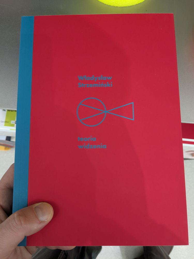 holding a book

Władysław Strzemiński - Teoria widzenia

(reddish with blueish spine margin & two triangles corner to corner, parallel outer edges, left triangle tightly circled...author name above, title below)

