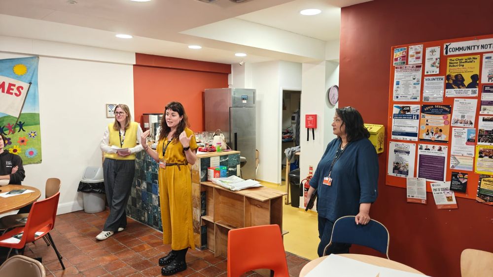 A photo of three people standing at the edge of a room, speaking to an audience out of shot