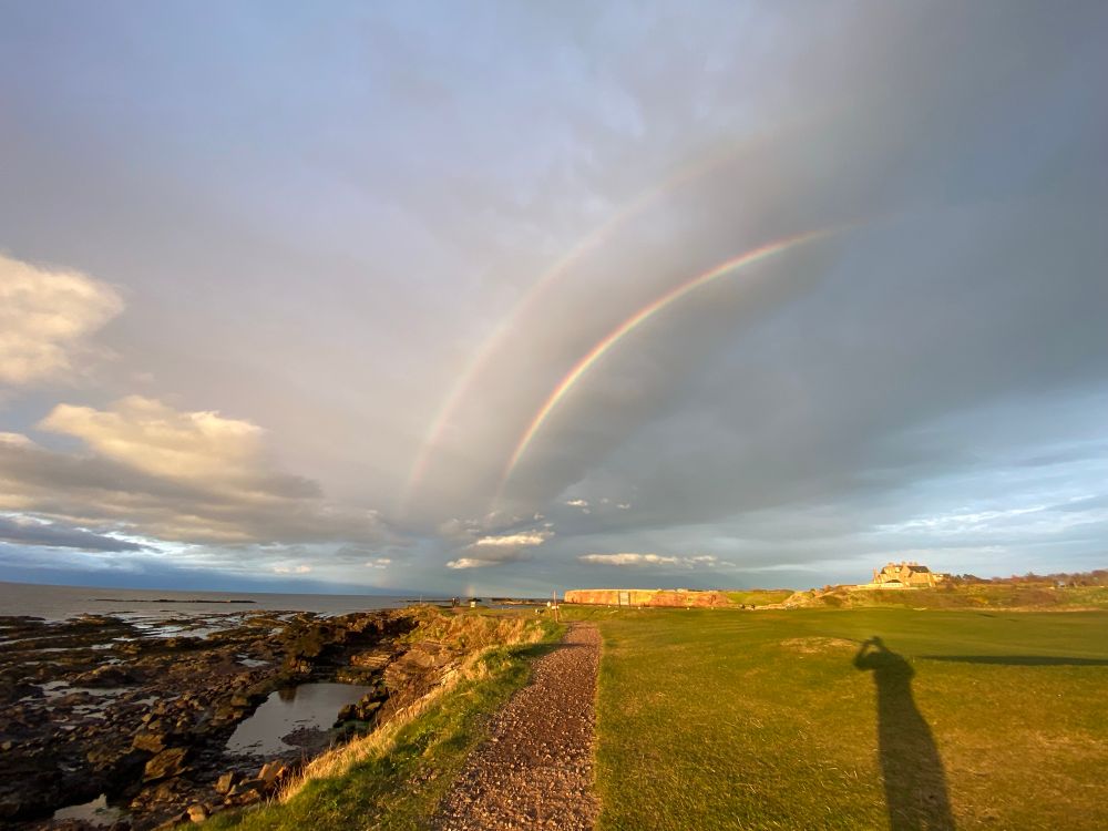 Double half rainbow over a golf course and a shoreline. 