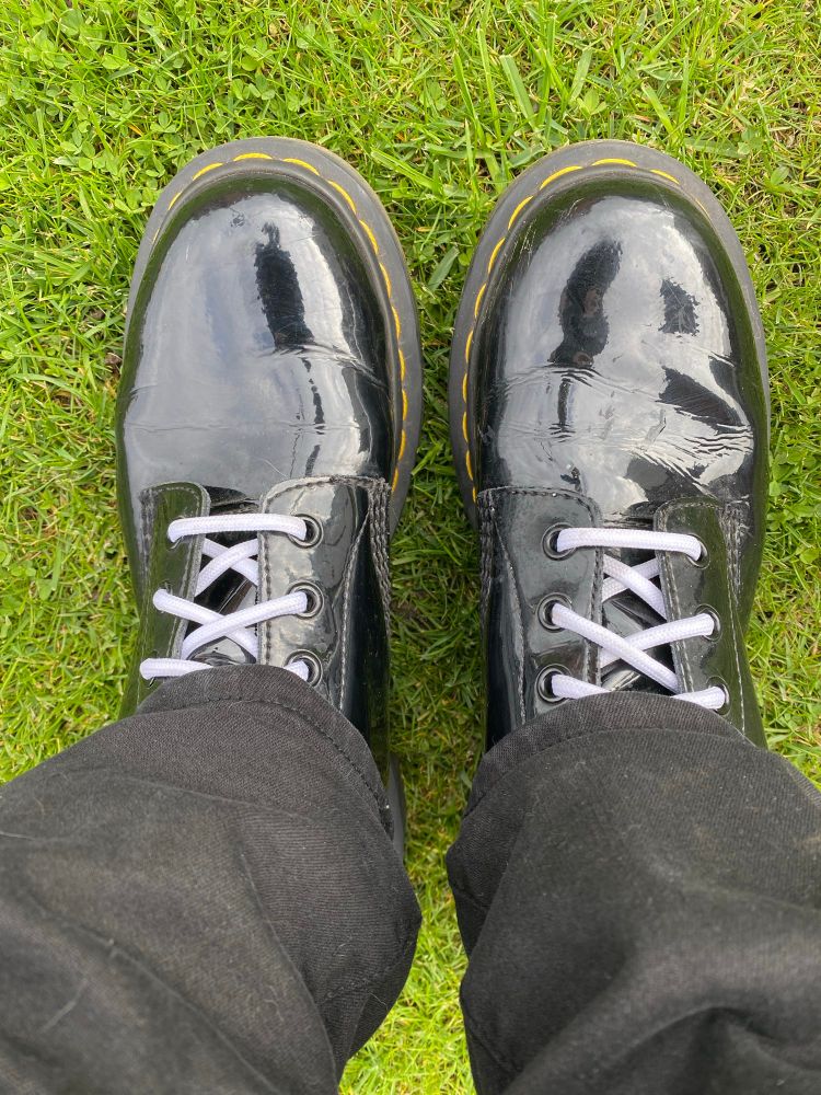 Patent black doc marten boots with white laces, standing on grass. 