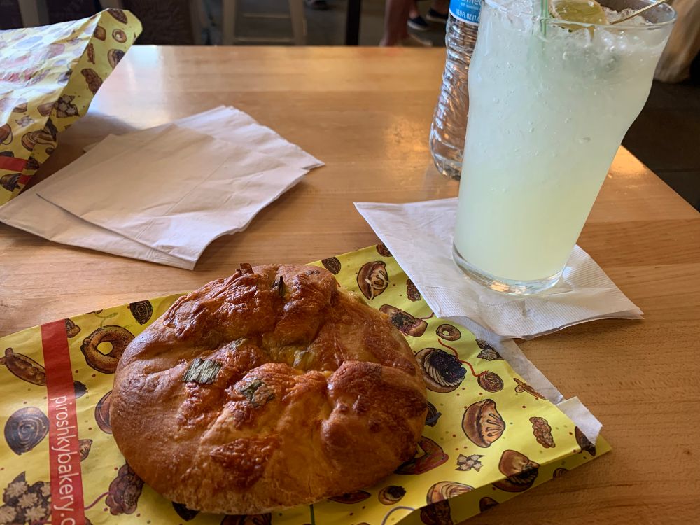 A cheesy piroshky (large filled pastry) on its wrapper next to a moscow mule cocktail.