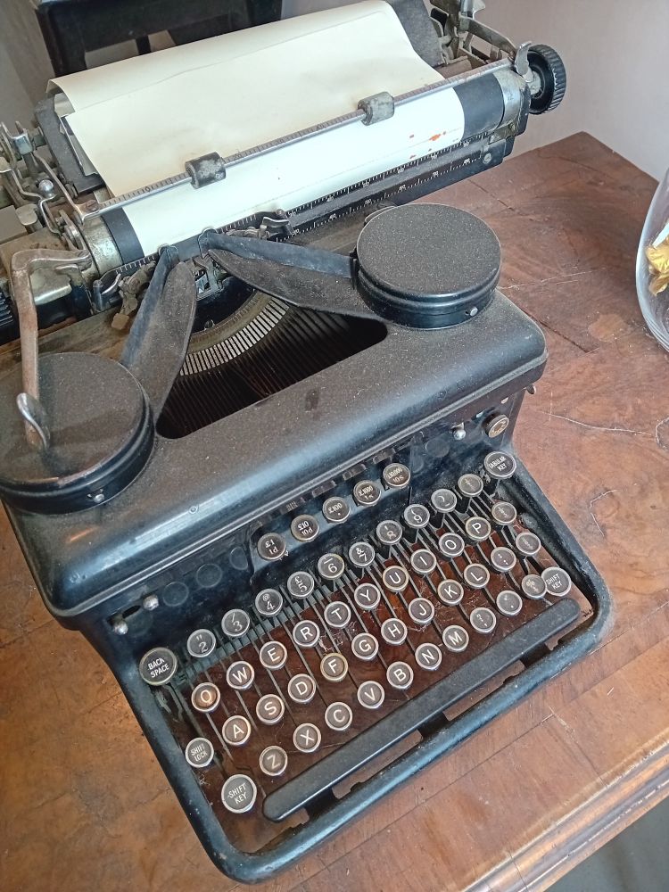 Old mechanical typewriter.
Dusty, black metal. Round keys in QWERTY format, with additional set of 5 GB currency (sterling - £sd) keys above.