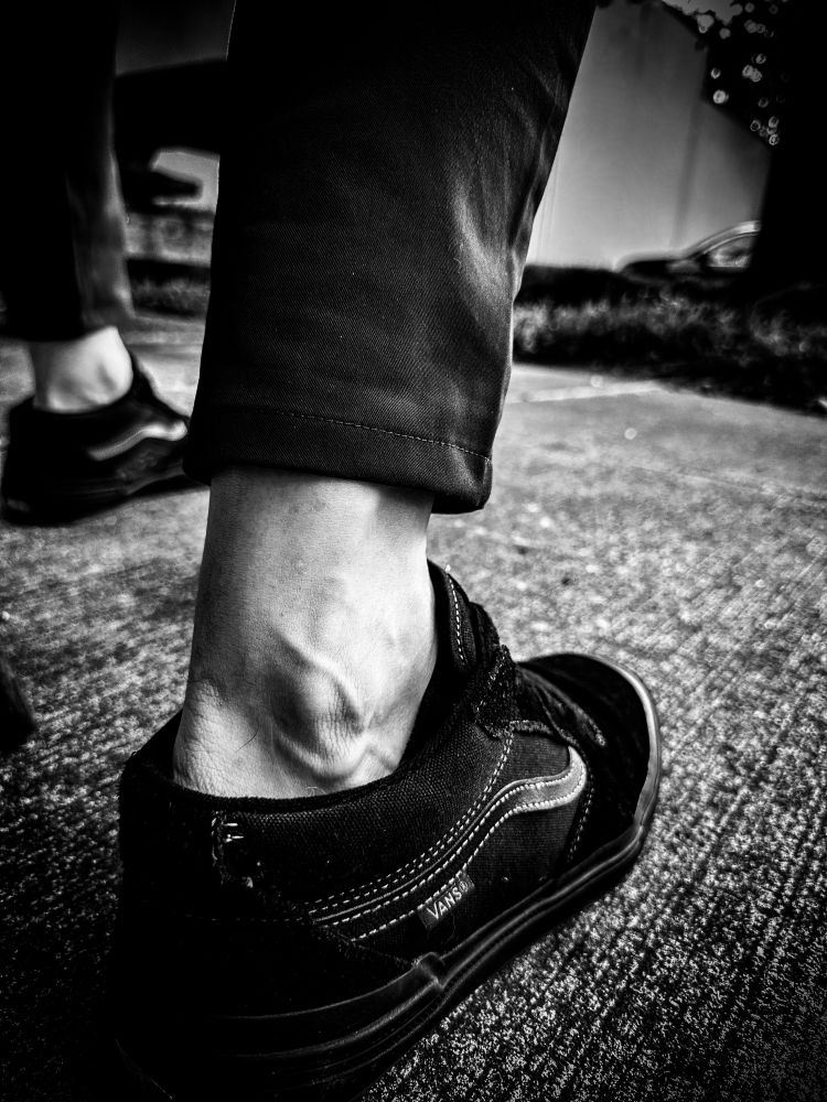 A black and white close-up photo of the photographers exposed ankles between his shoes and pants.