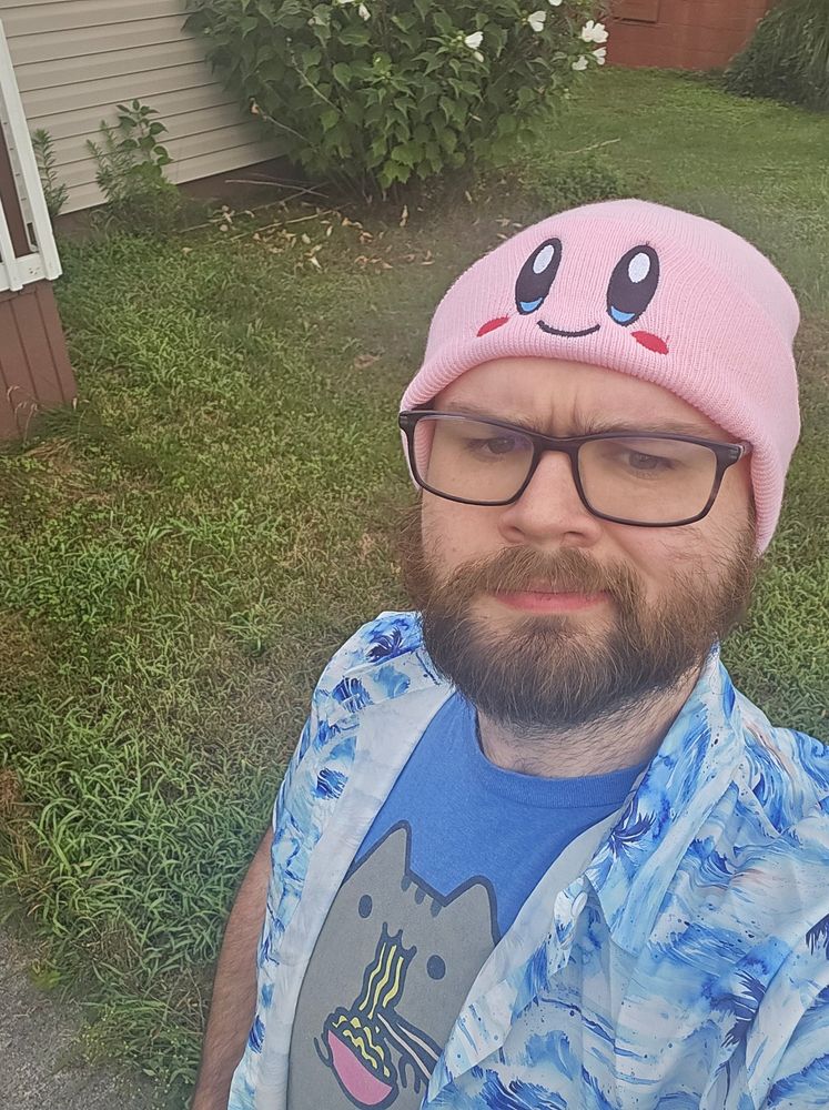 A selfie of jo wearing a kirby beanie and wearing a blue shurt with a cat eating noodles on it. He is handsome 💜