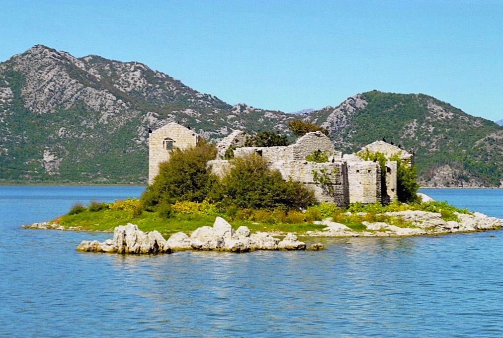 The ruins of an abandoned prison sit on a rocky island on a lake. In the distance is a mountain range.