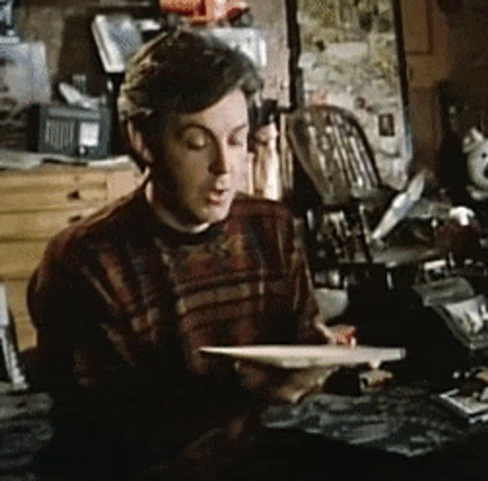 a man in a plaid sweater sits at a table holding a book