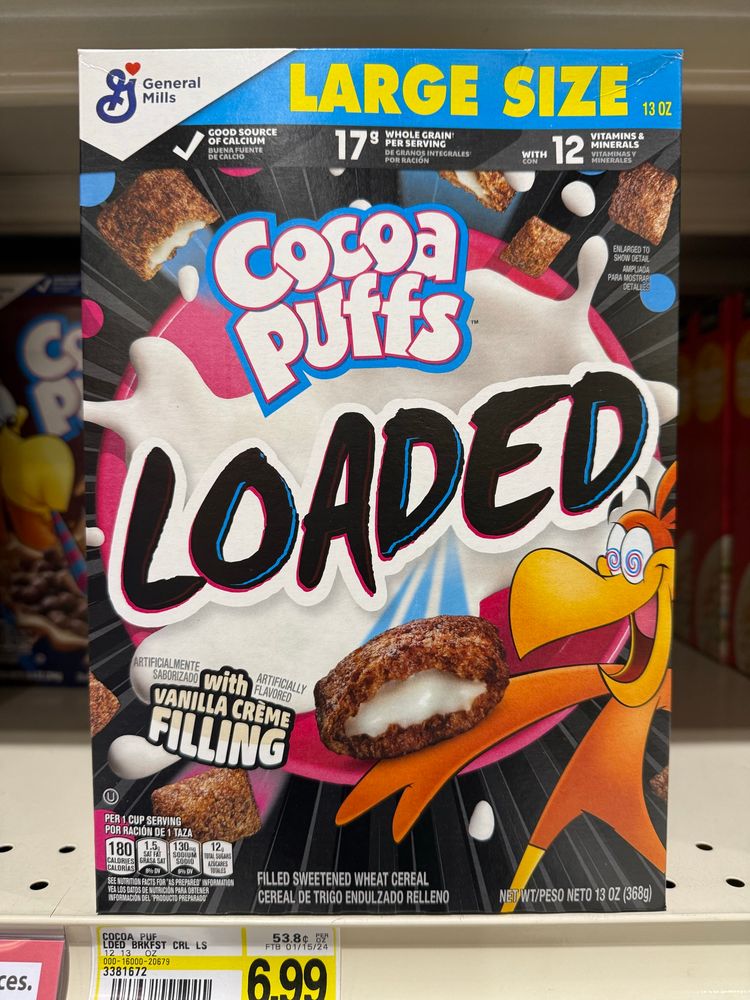 A box of “Cocoa Puffs Loaded” cereal which features the Cocoa Cuckoo looking ecstatically at a piece of cereal which has been split in half and is drippingly full of a white creamy substance that is oozing out of it. 