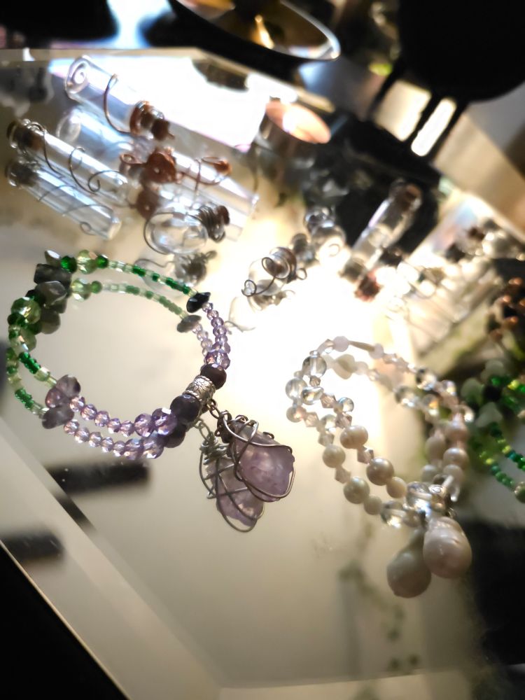 Handmade Jewelry by me and empty wrapped bottle pendants Displayed on a glass mirror.