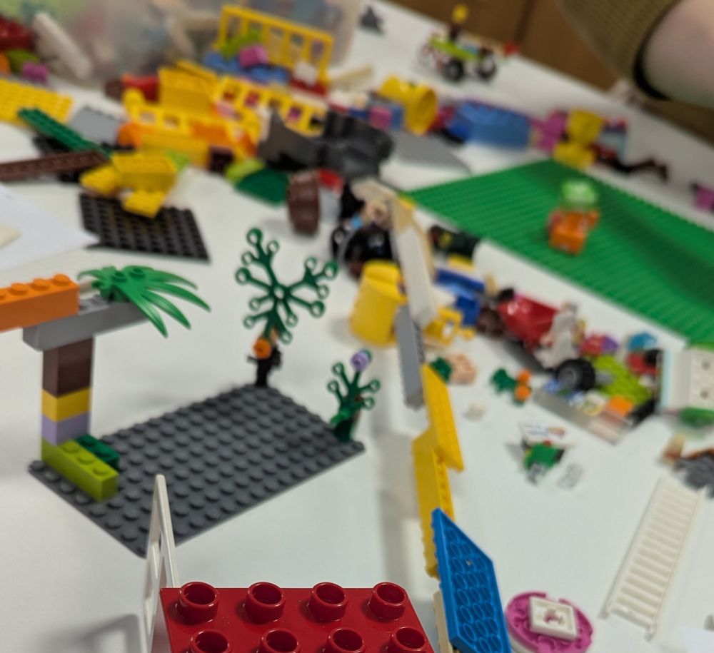 Mixed LEGO bricks scattered across table with some put together to represent trees. Most are blurred in background