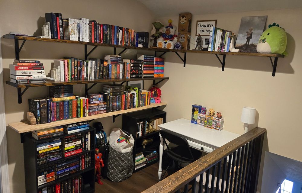 A small home library consisting of 4 floating shelves and two small free standing book shelves. The shelves are covered in books, funko pops, figurines, and pictures. Last time I checked, there was around 300 books! 