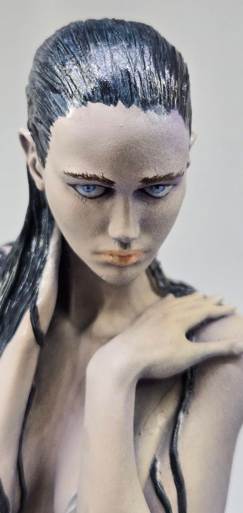 Close up of her face, looking directly at the camera.

Her nearly black hair is slicked back from her forehead, her right hand holding the back of her neck with wet hair cascading over it.

Her left hand sits on her left shoulder, and her gaze is a cross between demure, brazen, and defying.

She has blazing bright blue eyes, and a very pale complexion.