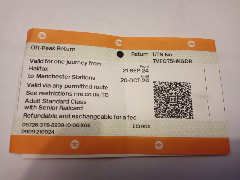 An off-peak return rail ticket from Halifax to Manchester Stations, with orange stripes at the top and bottom and further stripes with National Rail in tiny light green letters behind some of the text, though the central section with a QR code has a plain white background.