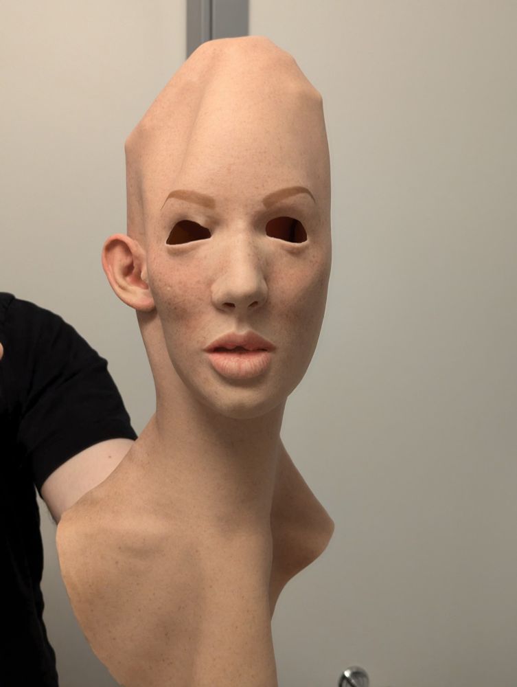 A person holding up an empty realistic silicone mask of a freckled light-skinned girl with attached neck.